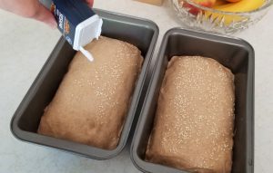 Sprinkling sesame seeds on top of bread dough in 2 pans.
