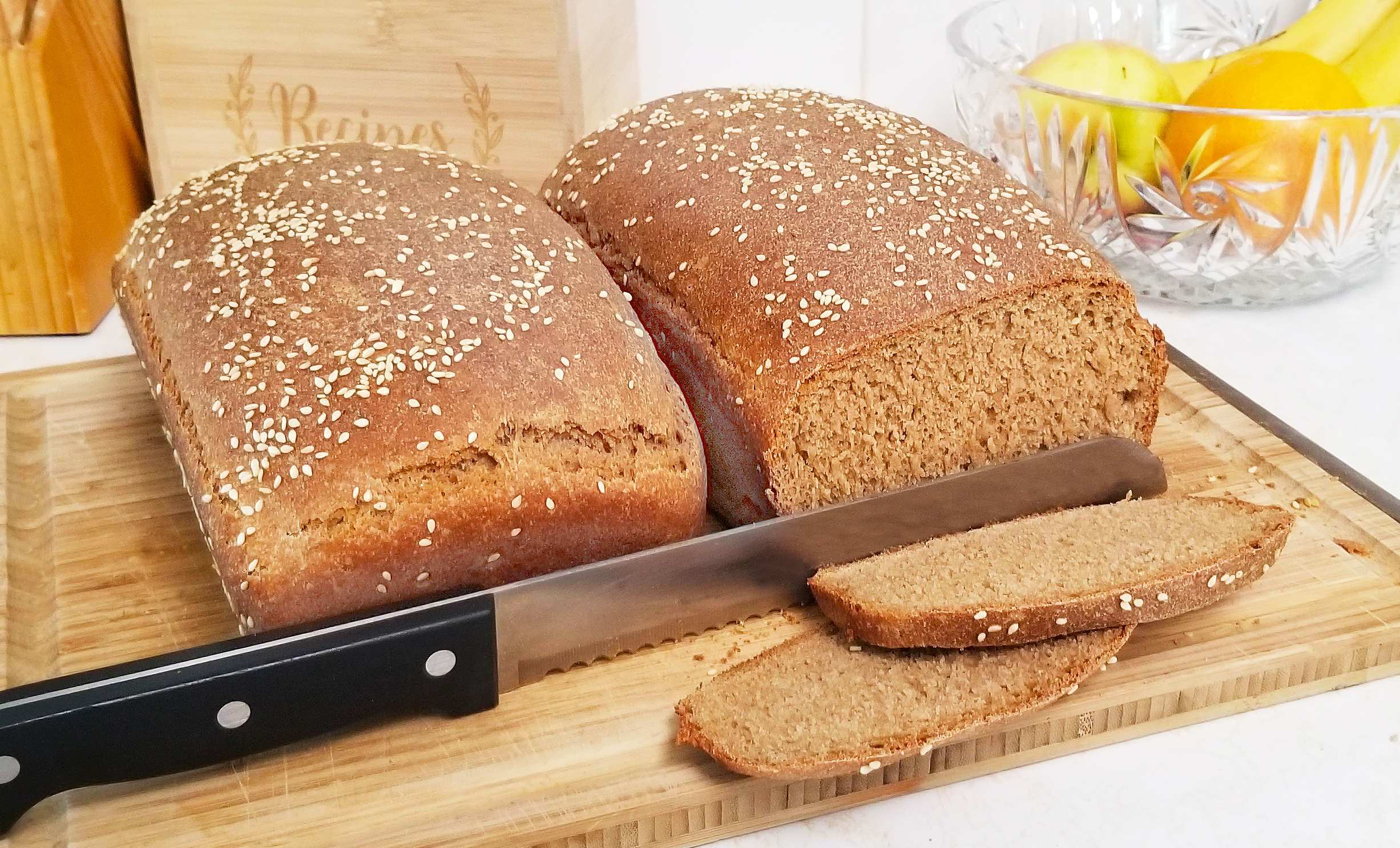 Two loafs of brown bread on a cutting board, with 2 slices cut from 1 loaf.